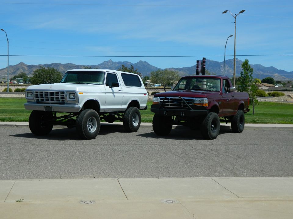 Lifted white 1979 Ford Bronco and maroon Ford F-150 pickup truck parked side-by-side.