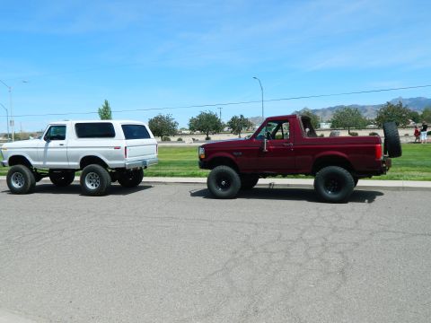 1979 Ford Bronco - A white Ford Bronco is parked on the left side of the frame, and a red Ford Bronco is parked on the right. Both vehicles are lifted with la…