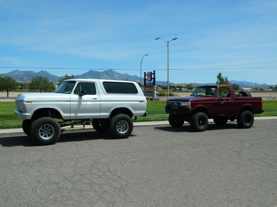 Lifted white 1979 Ford Bronco and lifted maroon Ford Bronco pickup truck parked side-by-side.