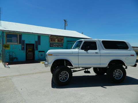 1979 Ford Bronco - A lifted white 1979 Ford Bronco is parked in front of a turquoise building labeled "Gateway Station Mini-Mart". The Bronco has large off-ro…