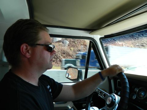 1979 Ford Bronco - Side profile of a man driving a vehicle, looking out the window at a rocky landscape and other vehicles on the road. The interior of the ve…