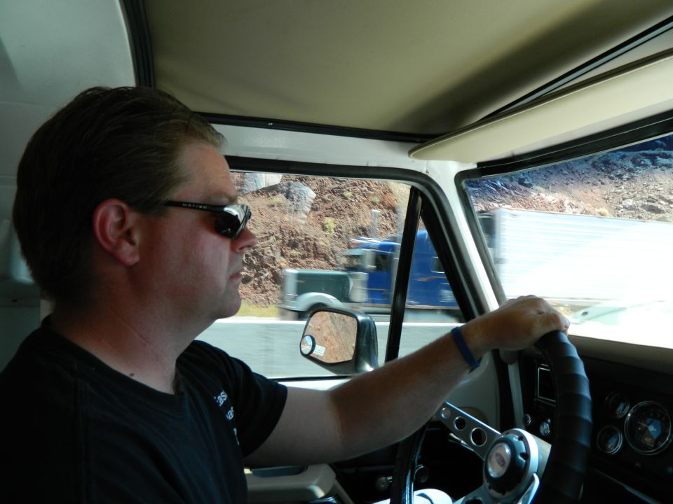 Man driving a vehicle, interior view showing steering wheel and dashboard, exterior view of road and landscape.