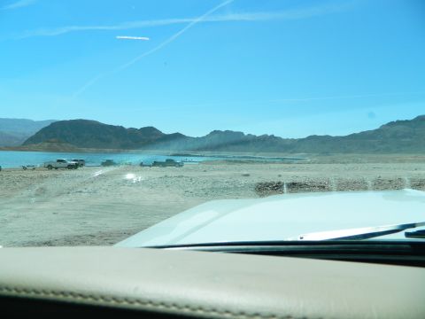 1979 Ford Bronco - A view from inside a vehicle looking out at a desert landscape with a large body of water and mountains in the distance. Several pickup tru…