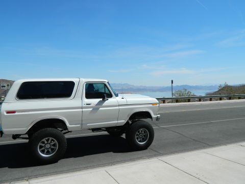 1979 Ford Bronco - A white 1979 Ford Bronco is parked on the side of a road with a scenic view of a large body of water and mountains in the background.