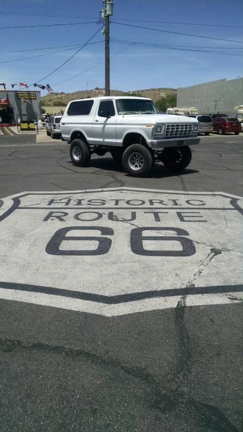 1979 Ford Bronco - A lifted white 1979 Ford Bronco is parked on a street with a painted Historic Route 66 shield in the foreground. The vehicle is viewed from…