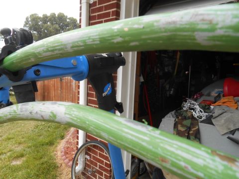 Green and white striped metal bar in foreground, blue and black bicycle repair stand behind, garage interior i