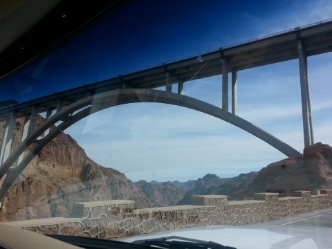 1979 Ford Bronco - A wide concrete arch bridge spans across a canyon under a bright blue sky. Rocky mountains are visible in the distance, and a stone wall li…