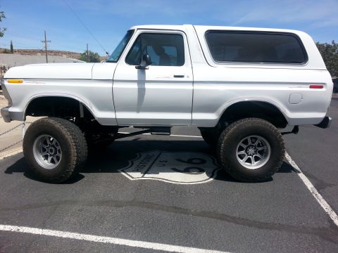 1979 Ford Bronco - A lifted white 1979 Ford Bronco is parked on a road marked with a Historic U.S. Route 66 emblem.