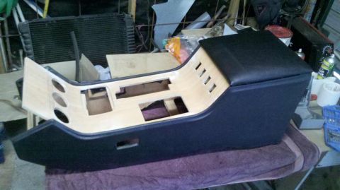1982 Ford Bronco - A custom center console with a woodgrain finish and black upholstered armrest is shown in a workshop setting. The console has cutouts for s…