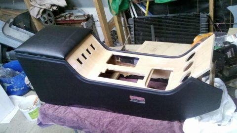 1982 Ford Bronco - A custom-built center console with a black upholstered top and unfinished wood interior is shown in a workshop setting. The console feature…