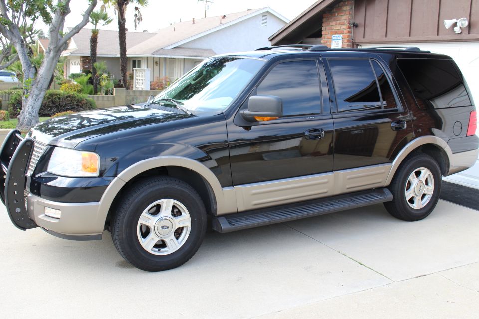 Black Ford Expedition SUV with tan trim parked on a concrete driveway.