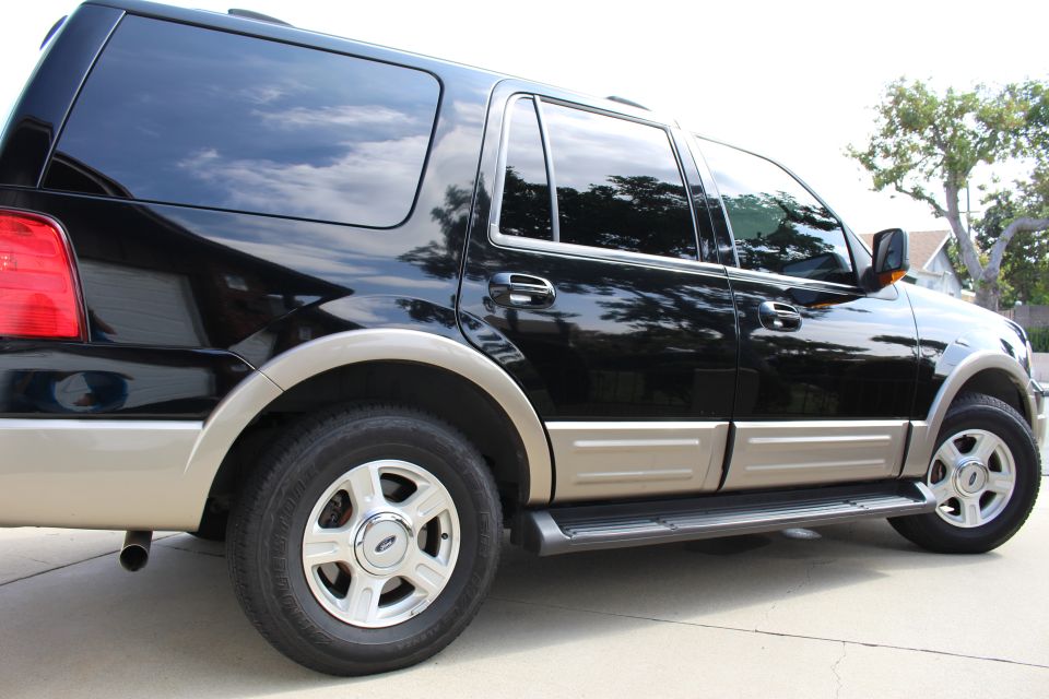 Black Ford Expedition SUV, right side view, two-tone paint, chrome wheels, parked on concrete.