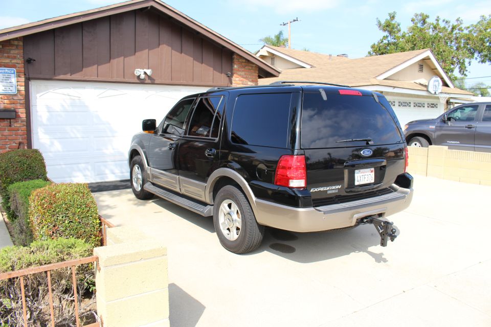 Black Ford Expedition SUV with beige lower trim and trailer hitch parked in front of a garage.