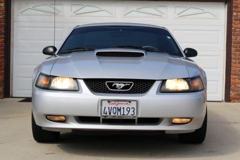 2002 Ford Mustang - Front view of a silver Ford Mustang parked in front of a white garage door. The car has its headlights on and a California license plate re…