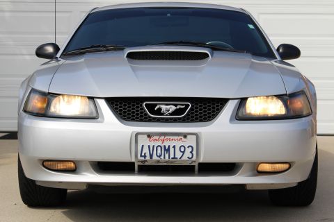 2002 Ford Mustang - Front view of a silver Ford Mustang with its headlights on. The California license plate reads "4VQM193".