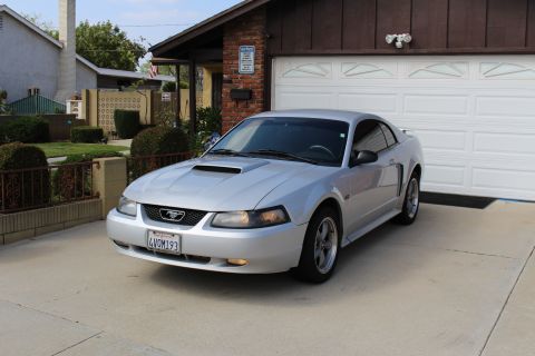 2002 Ford Mustang - A silver Ford Mustang coupe is parked in a driveway in front of a white garage door. The car is viewed from a 3/4 front angle, showing its…