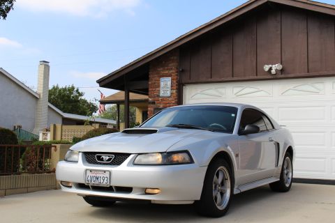 2002 Ford Mustang - A silver 2002 Ford Mustang GT is parked in front of a house with a white garage door. The car has a California license plate that reads "4V…