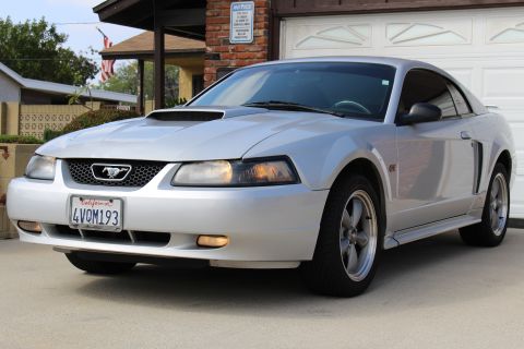 2002 Ford Mustang - The front 3/4 view of a silver 2002 Ford Mustang GT coupe is parked in a driveway in front of a garage. The car features a black honeycomb…