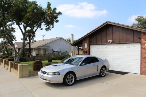 2002 Ford Mustang - A silver 2002 Ford Mustang coupe is parked in front of a suburban garage. The car is viewed from a 3/4 front angle, showcasing its sleek de…