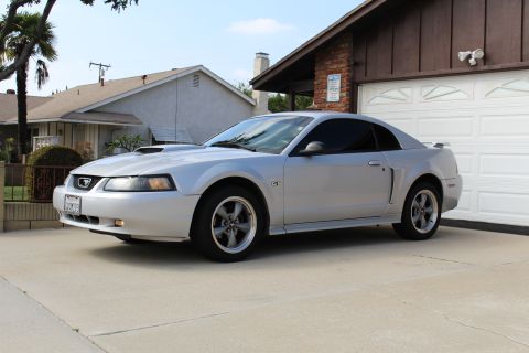 2002 Ford Mustang - A silver 2002 Ford Mustang GT coupe is parked in a driveway in front of a residential garage. The car is viewed from a 3/4 front angle, sho…
