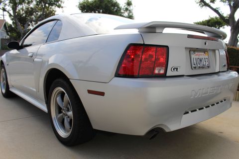 2002 Ford Mustang - The rear quarter view of a silver Ford Mustang GT shows its taillights, spoiler, and California license plate. The car is parked on a concr…