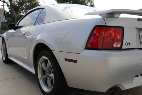 2002 Ford Mustang - The rear quarter panel and taillight of a silver Ford Mustang GT are shown in a side view. The car has a rear spoiler and a GT badge on the…