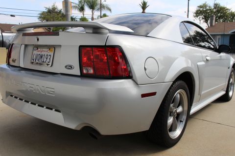 2002 Ford Mustang - The rear passenger side quarter view of a silver Ford Mustang coupe is shown. The car features a rear spoiler, a California license plate r…