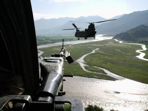 1981 Ford Bronco - A view from a helicopter gunner's position shows a second helicopter flying over a winding river in a mountainous valley.