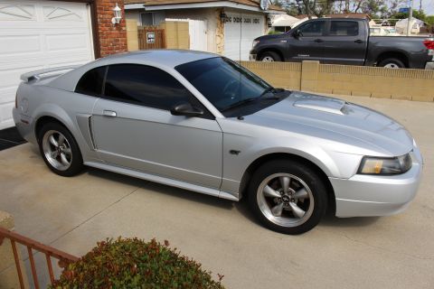 2002 Ford Mustang - A silver 2002 Ford Mustang GT coupe is parked in a driveway. The car has tinted windows and a rear spoiler.