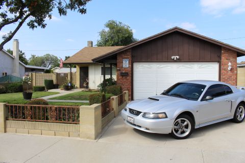 2002 Ford Mustang - A silver 2002 Ford Mustang coupe is parked in the driveway of a single-story house with a white garage door.