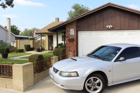 2002 Ford Mustang - A silver 2002 Ford Mustang GT coupe is parked in a driveway in front of a brick and wood-sided garage. The car is viewed from a 3/4 front a…