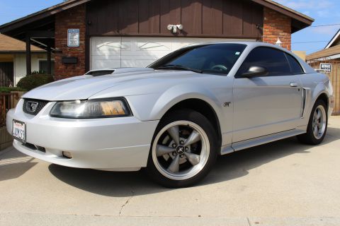 2002 Ford Mustang - A silver 2002 Ford Mustang GT is parked in front of a garage. The car is shown from a 3/4 front angle, highlighting its sporty design and c…