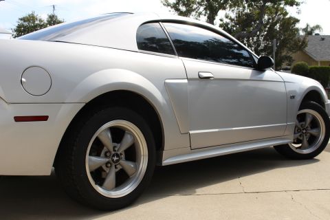 2002 Ford Mustang - The rear quarter panel and side of a silver 2002 Ford Mustang GT coupe is shown in a three-quarter rear view. The car is parked on a concre…