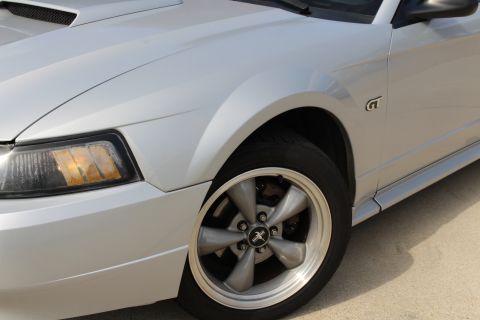 2002 Ford Mustang - Close-up of the front fender, headlight, and wheel of a silver Ford Mustang GT. The vehicle has a silver five-spoke wheel with a black cent…