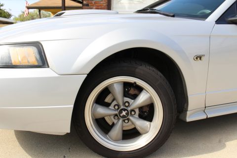 2002 Ford Mustang - Close-up of the front fender and wheel of a silver Ford Mustang. The vehicle features a silver 5-spoke wheel with a black and red Mustang e…