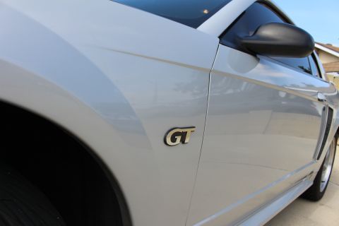 2002 Ford Mustang - A close-up side view of a silver Ford Mustang GT shows the emblem on the fender and the side mirror. The car is parked outdoors on a sunny…