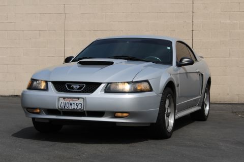 2002 Ford Mustang - Front 3/4 view of a silver Ford Mustang parked in front of a beige brick wall. The car has a California license plate that reads "4VQM193".