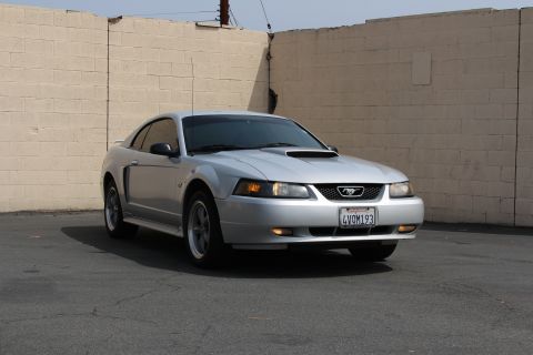 2002 Ford Mustang - A silver Ford Mustang is parked outdoors in front of a textured wall. The car's front end is visible, including the grille and headlights.