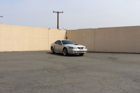2002 Ford Mustang - A silver 2002 Ford Mustang is parked in an outdoor lot with a tan wall in the background.