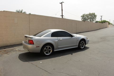 2002 Ford Mustang - Silver 2002 Ford Mustang coupe seen from a 3/4 front angle with a tan brick wall in the background.