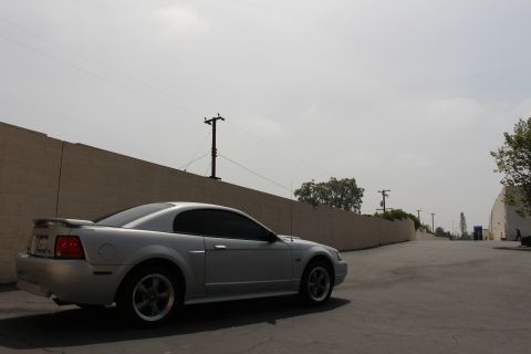 2002 Ford Mustang - Silver 2002 Ford Mustang coupe parked on asphalt with a wall in the background.