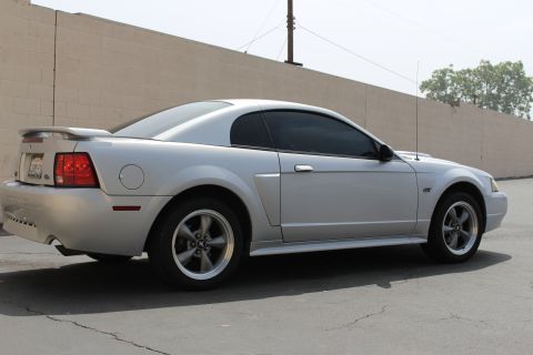2002 Ford Mustang - A silver 2002 Ford Mustang coupe is parked outdoors, showing its side profile against a neutral wall.