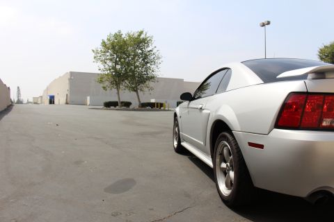 2002 Ford Mustang - A silver 2002 Ford Mustang coupe is parked in an industrial area, viewed from the rear three-quarter angle.