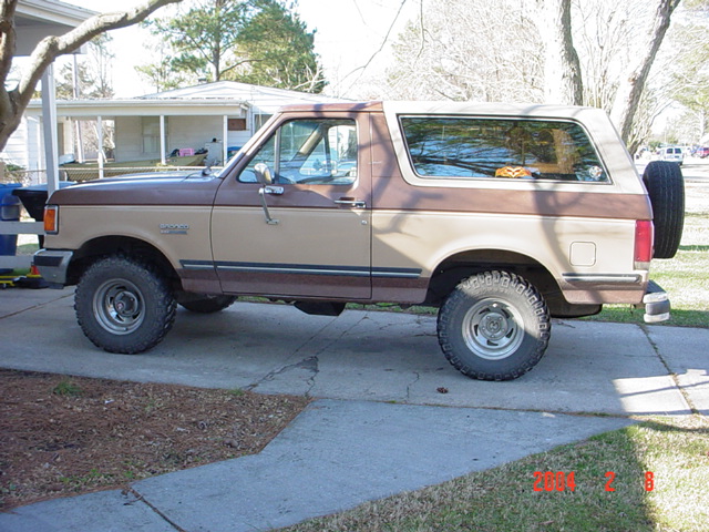 Side view of a two-tone tan and brown Ford Bronco SUV parked in a driveway with rear-mounted spare tire