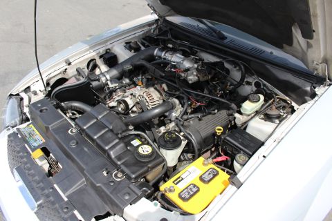 2002 Ford Mustang - The engine bay of a 2002 Ford Mustang is shown, a prominent yellow battery and various engine components.