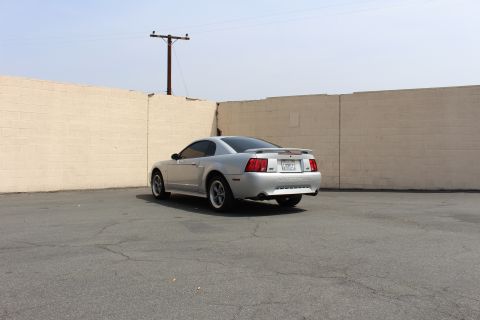 2002 Ford Mustang - A silver 2002 Ford Mustang coupe is parked in an empty lot with a brick wall in the background.