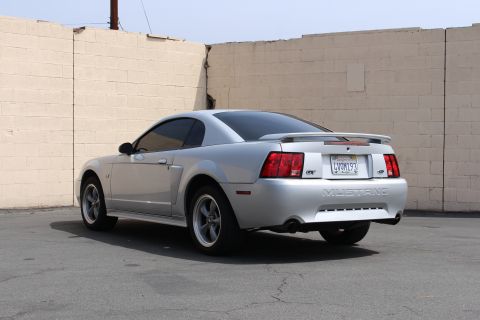 2002 Ford Mustang - This silver 2002 Ford Mustang GT coupe is shown from the rear, parked outdoors near a textured brick wall.