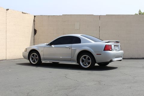 2002 Ford Mustang - A silver 2002 Ford Mustang coupe is parked outdoors in front of a textured wall.