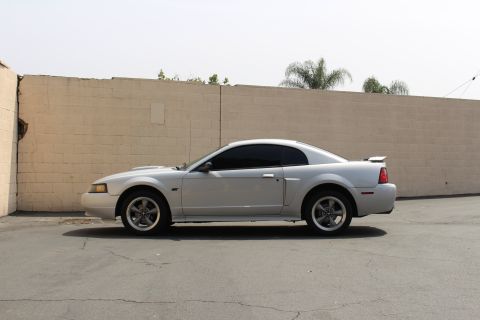 2002 Ford Mustang - A silver 2002 Ford Mustang coupe is shown from the side, parked in front of a textured brick wall.