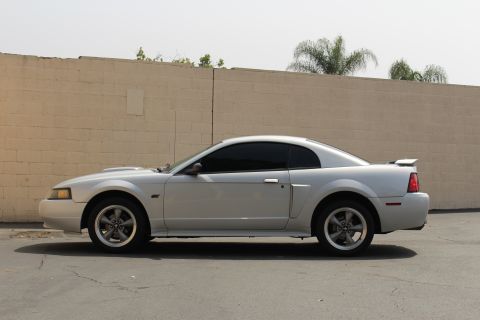 2002 Ford Mustang - A silver 2002 Ford Mustang coupe is shown from the side, parked in front of a brick wall.